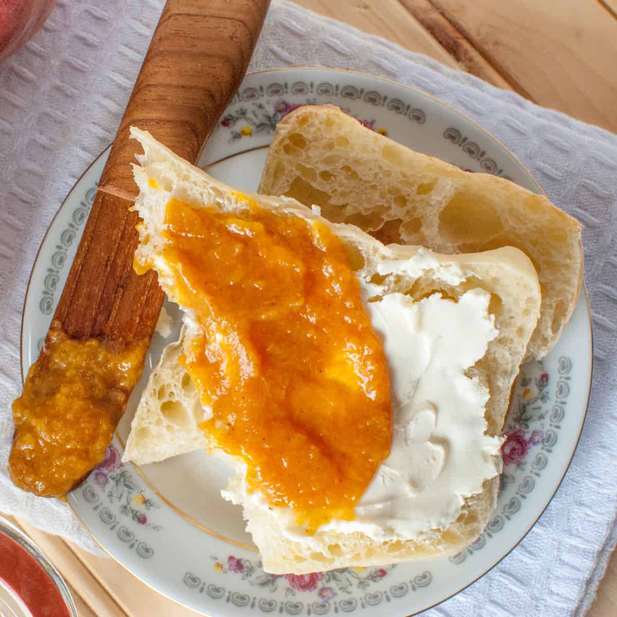 Crockpot Peach Butter on a piece of bread next to a wooden knife on a white plate