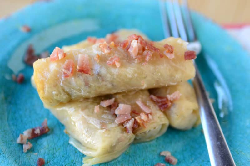 slow cooker Cabbage rolls garnished with bacon on a blue plate next to a silver fork