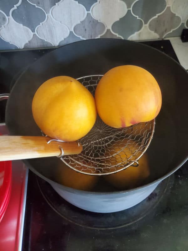 Peaches in a spider strainer going into a pot of water