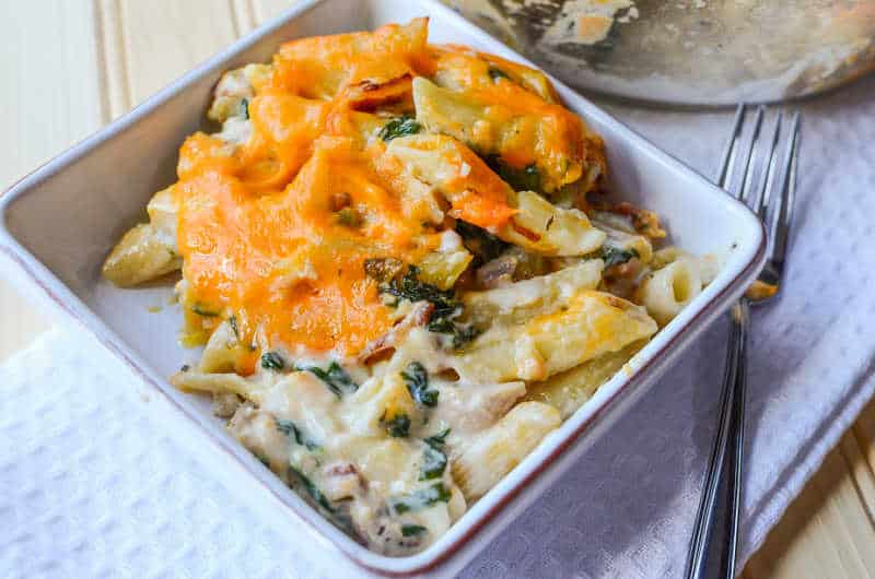 cheesy pasta casserole in a white bowl next to the serving dish and a fork