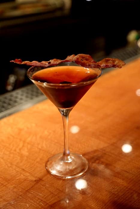 Bacon strip on a cocktail in a martini glass on a wooden counter 