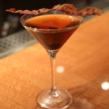 Bacon Manhattan in a martini glass with a slice of bacon for garnish