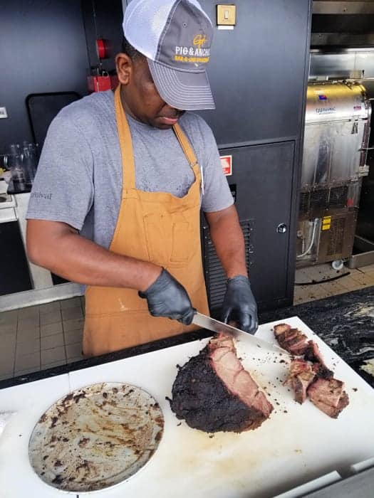 Man holding a knife cutting a piece of barbecued meat on a white cutting board