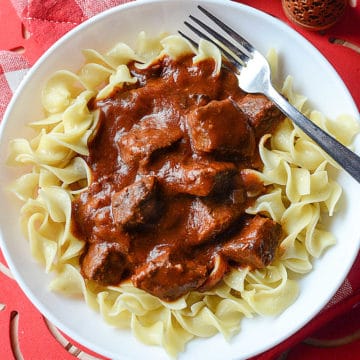 crockpot goulash on a white plate with egg noodles and a fork