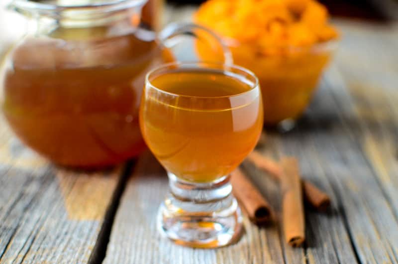 Small glass of slow cooker pumpkin spice liqueur on a wooden background with pumpkin in the background