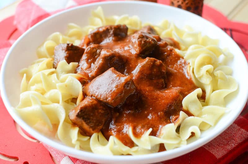 goulash beef over egg noodles on a white plate