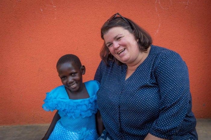 Tammilee and a young girl in a blue dress by an orange wall