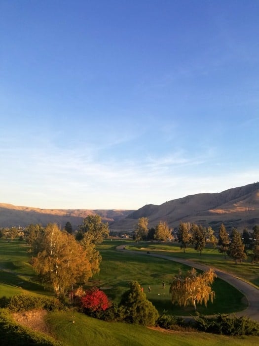 Looking out over a golf course with trees and rolling brown hills in the background 