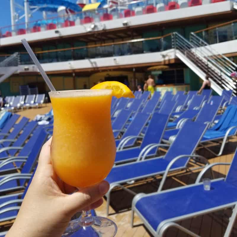 Carnival Cruise Lines Mango Magic Cocktail held in front of blue pool chairs