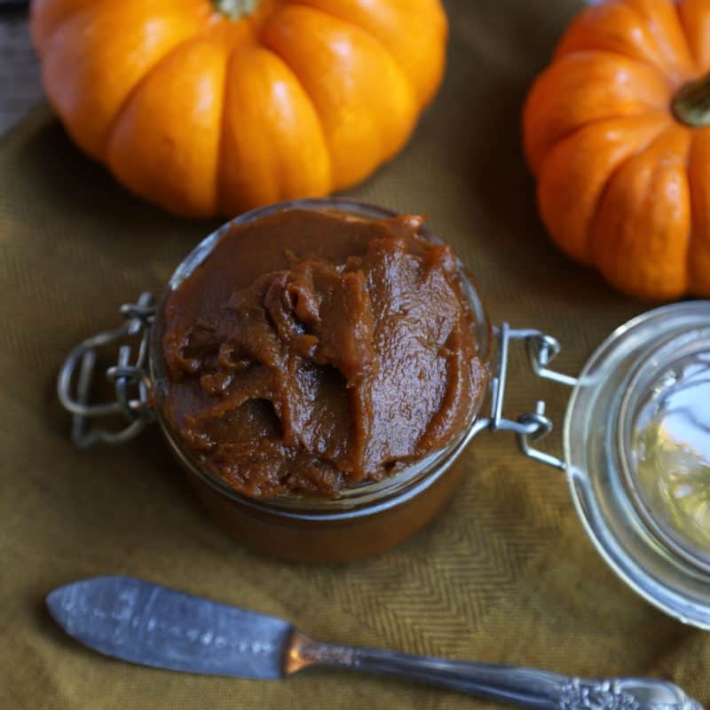 Crock Pot Pumpkin Butter in a glass lidded jar next to pumpkins and a silver knife