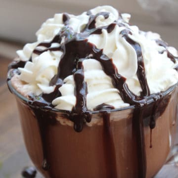 Crockpot hot chocolate in a glass mug topped with whipped cream and chocolate syrup