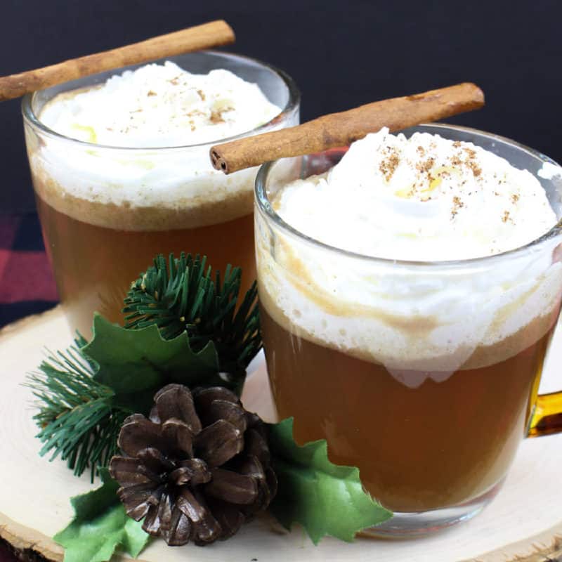 Hot Buttered Rum in glass coffee mugs with cinnamon sticks on a wood board
