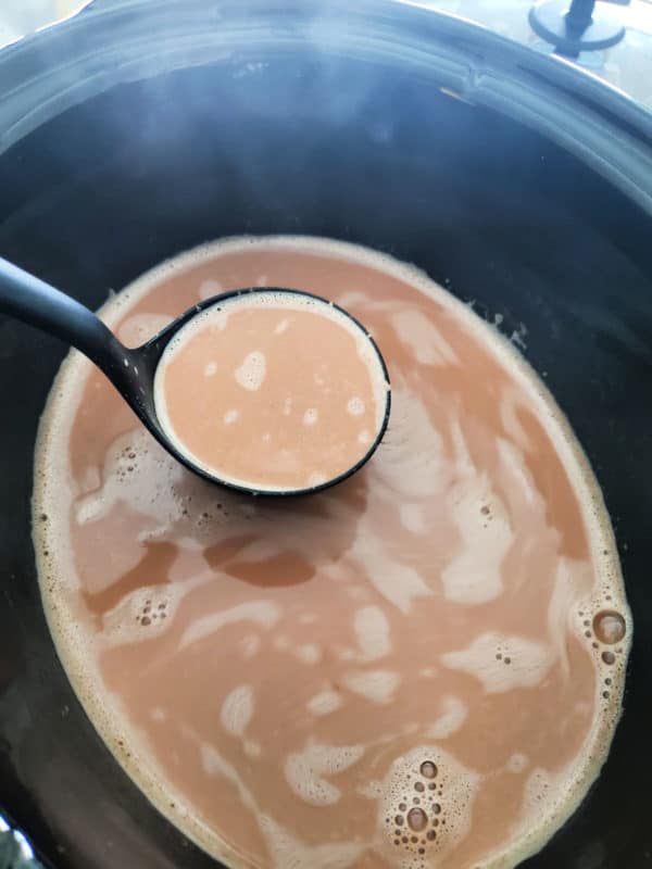 Ladle filled with hot chocolate above a slow cooker 