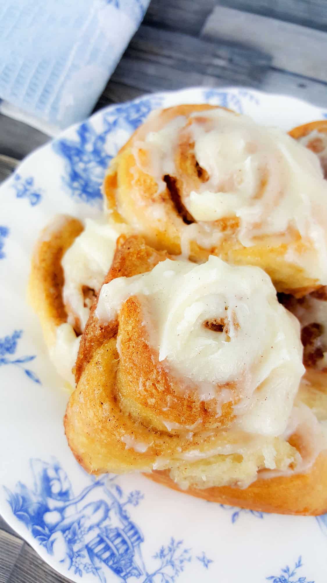 close up of iced cinnamon rolls on a white and blue plate