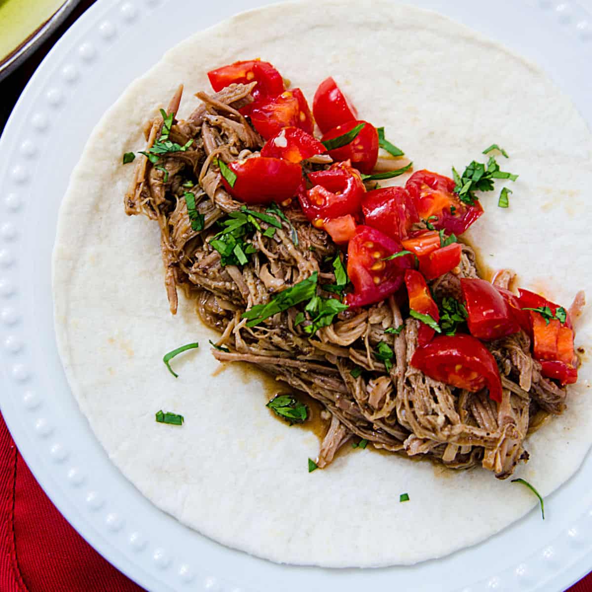 Mexican Pulled Pork, tomatoes, onions, on a tortilla on a white plate.