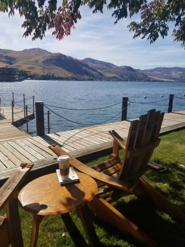 Adirondack chair and table near the lake and a dock with mountains in the background