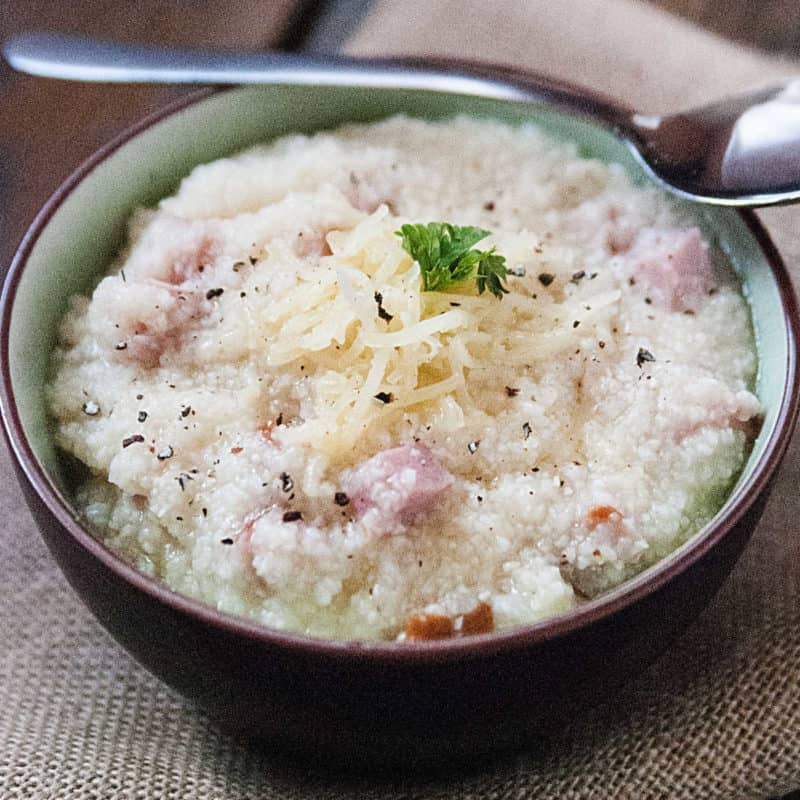 Ham and cheese grits in a bowl with silver spoon.