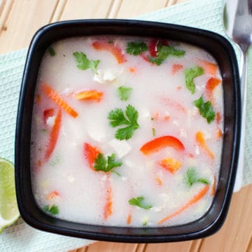 Thai Coconut milk chicken soup in a dark bowl next to a spoon