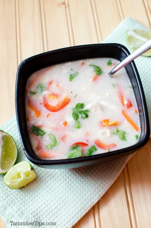 Thai chicken soup in a dark bowl on a cloth napkin with limes