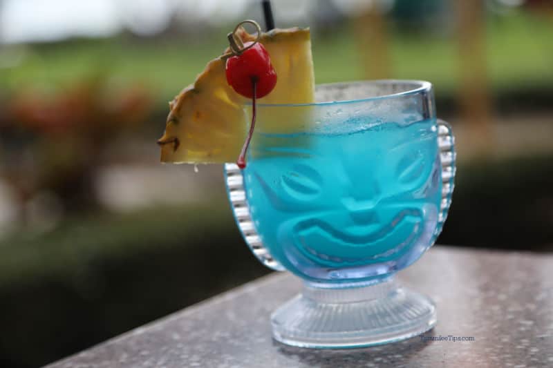 Tiki glass with a blue drink, pineapple cherry garnish, with a tropical background