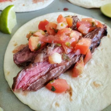 Carne Asada street taco on a baking sheet with lime wedges.