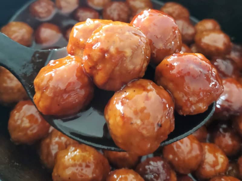 Grape Jelly Meatballs on a black spoon coming out of the crockpot. 