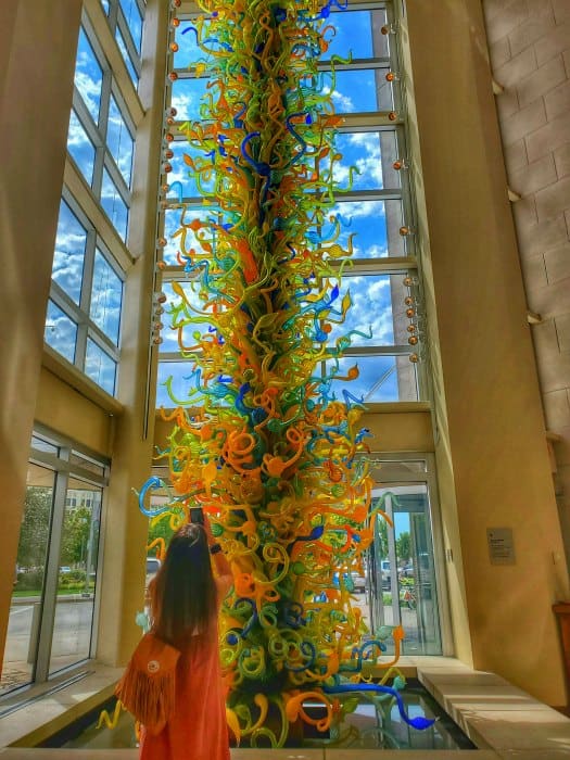 Amy taking a photo of the Chihuly glass sculpture with windows around it. 