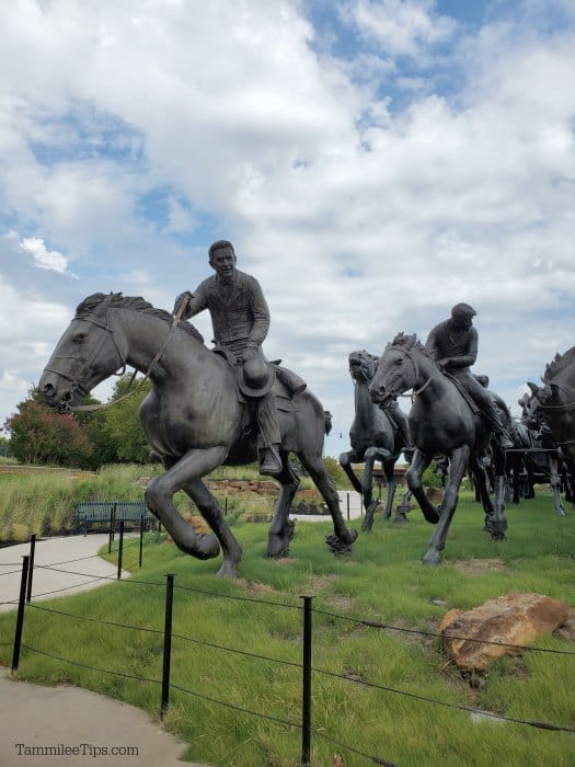 large sculpture of horse and riders on a grassy field