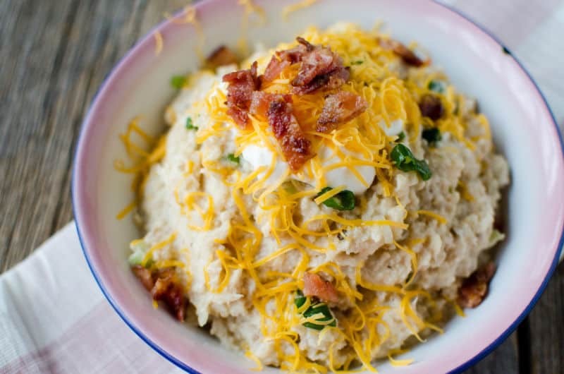 Slow Cooker Cauliflower mashed with bacon and cheese on top of it in a white bowl with blue pink rim