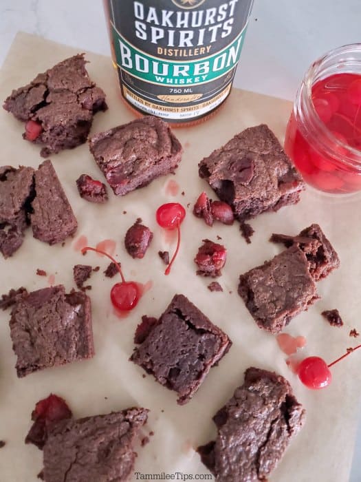 Bourbon Cherry Chocolate Brownies on parchment paper with a bottle of Oakhurst Spirits Bourbon Whiskey in the background