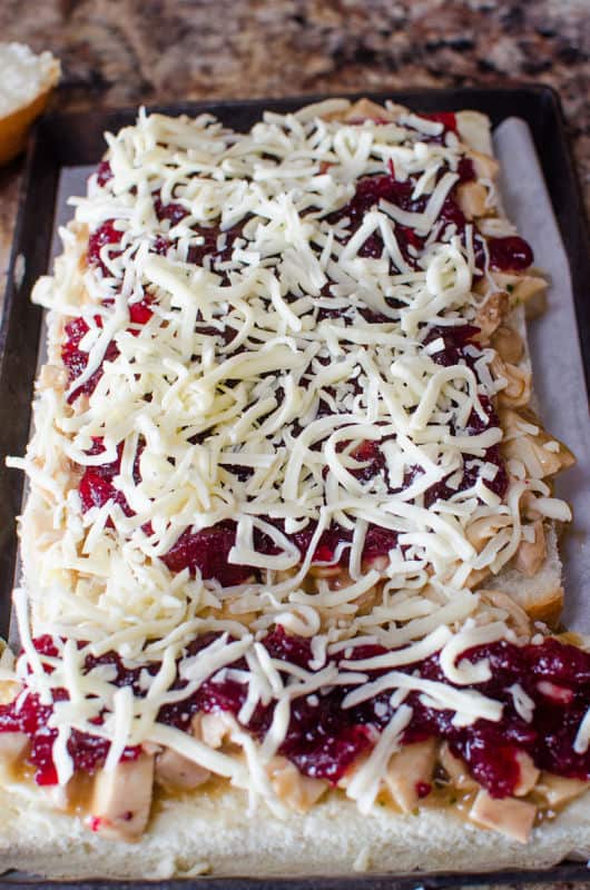 cranberry and cheese on top of turkey gravy layer on the bottom layer of slider buns on a baking dish. 