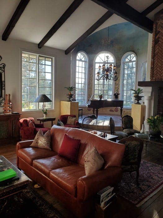 leather couch with pillows near a piano, chandelier, and large picture windows. 