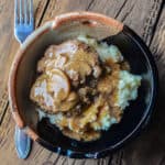 Salisbury steak over potatoes in a pottery bowl next to a fork