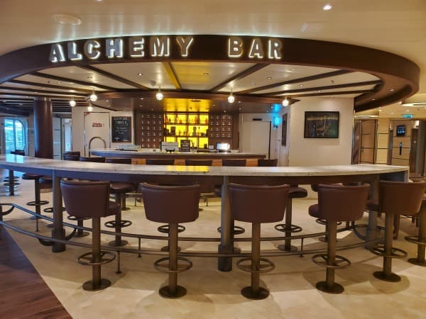 bar stools and counters with a bar behind it. Alchemy Bar sign over the bar