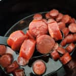 a slow cooker bowl with a spoon lifting cut kielbasa