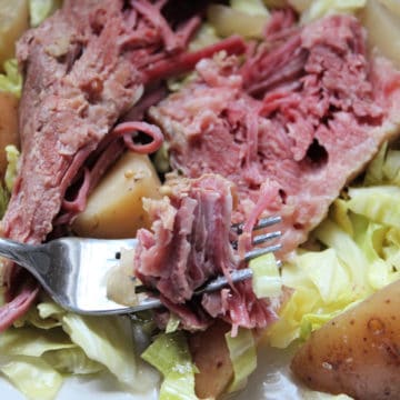 Crockpot Corned Beef and Cabbage on a white plate with potatoes, piece of corned beef on a fork