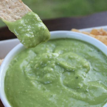 Avocado salsa in a white bowl with a tortilla chip dipping into it.