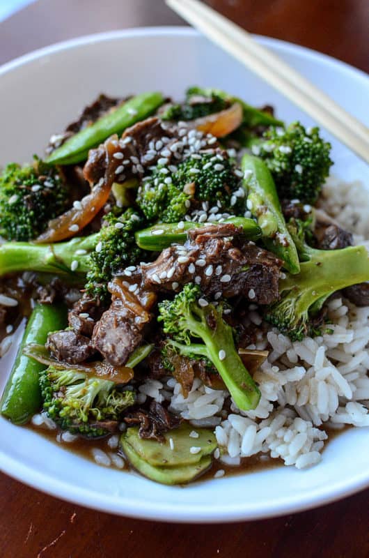 Beef and broccoli over white rice in a bowl with chopsticks