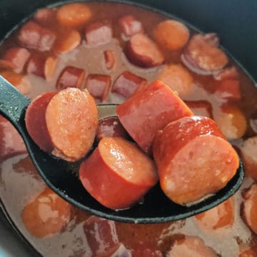 Crockpot barbecue beer kielbasa on a spoon coming out of the slow cooker bowl