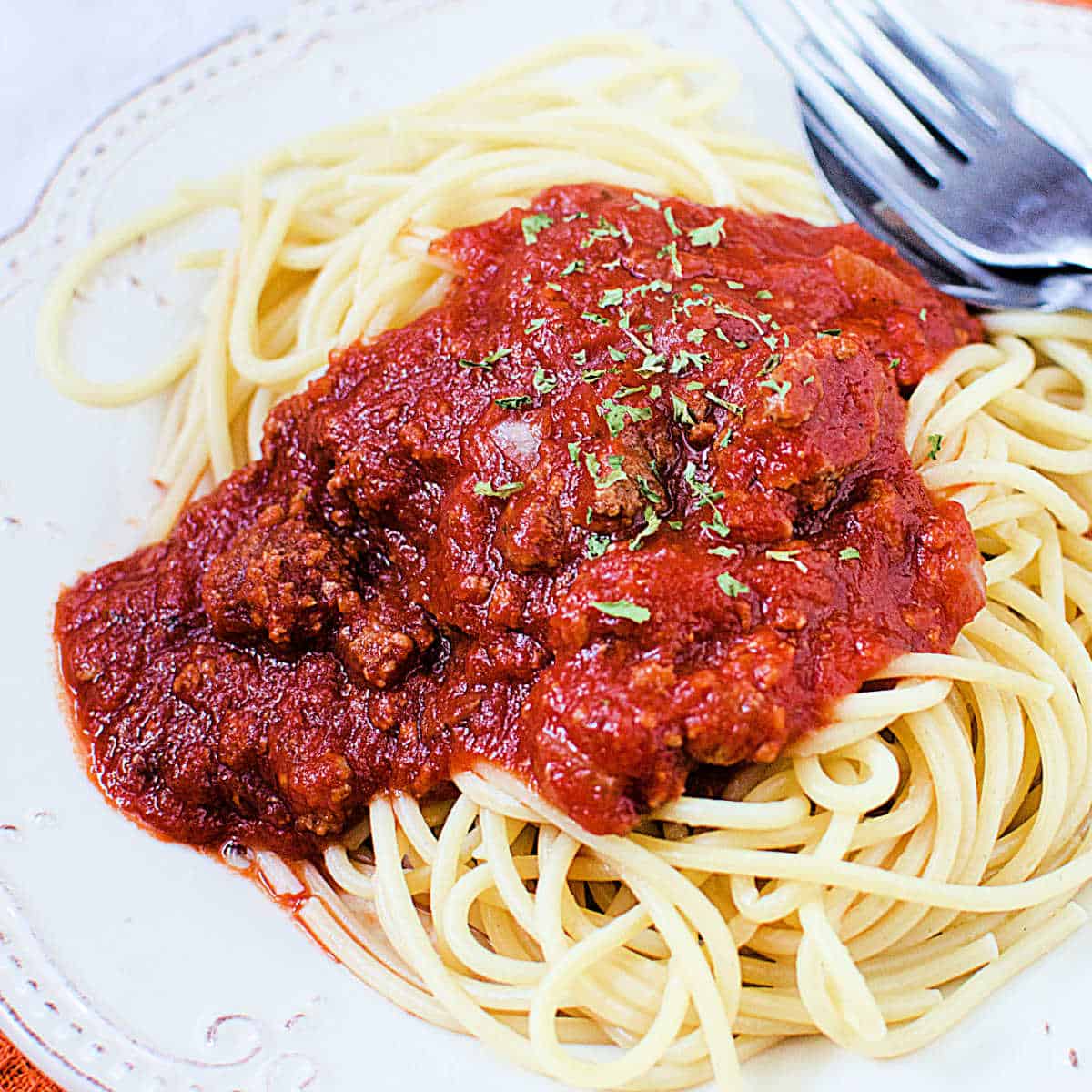 Crock Pot Bolognese Sauce on top of spaghetti noodles next to a fork on a white plate