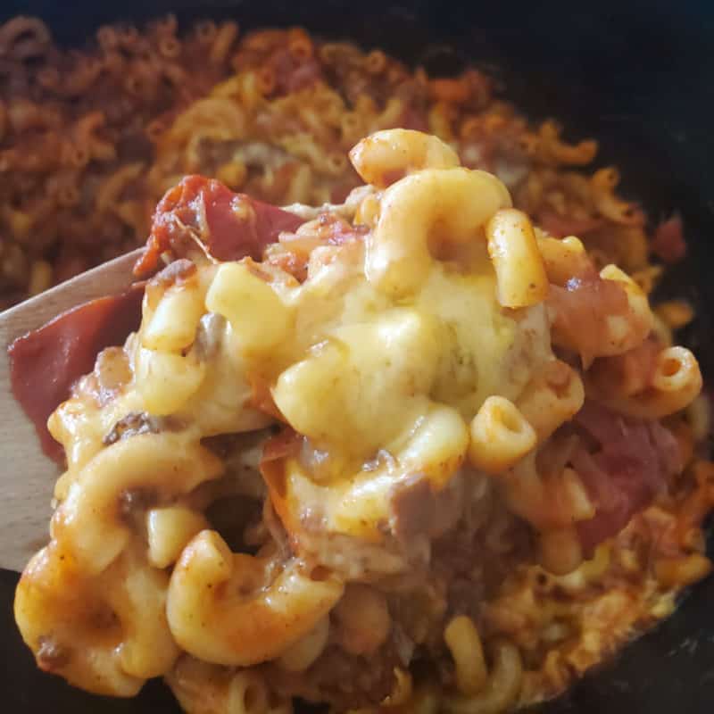 Chili mac and cheese on a wooden spoon over a slow cooker