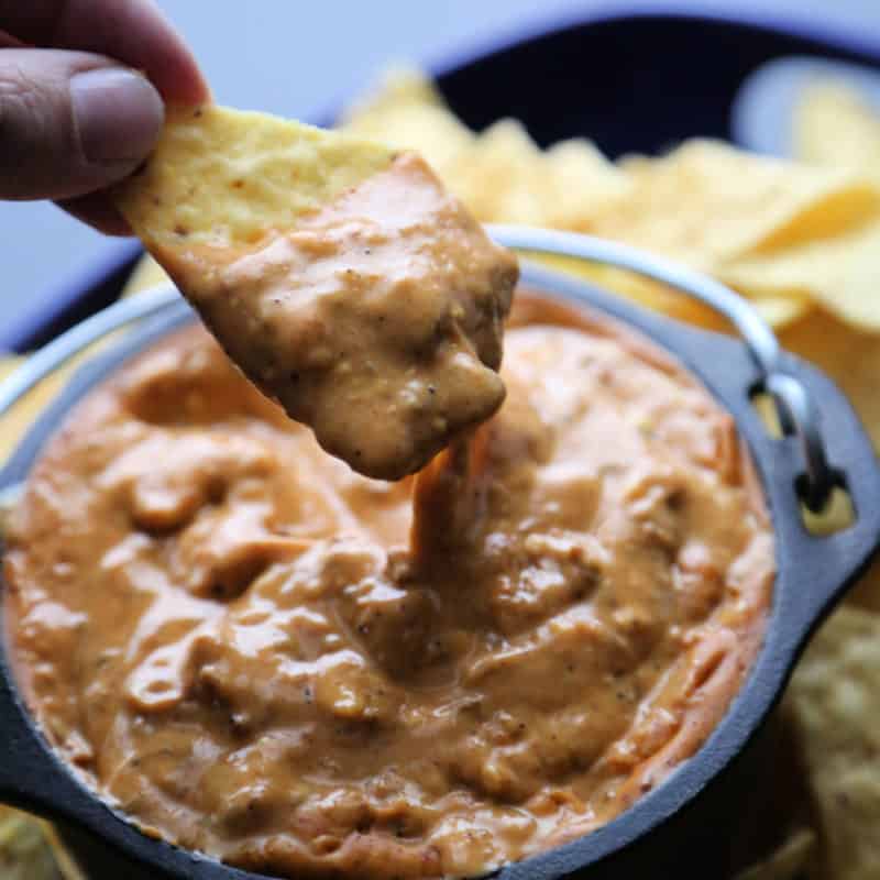 hand holding a chip dipping into chili's queso