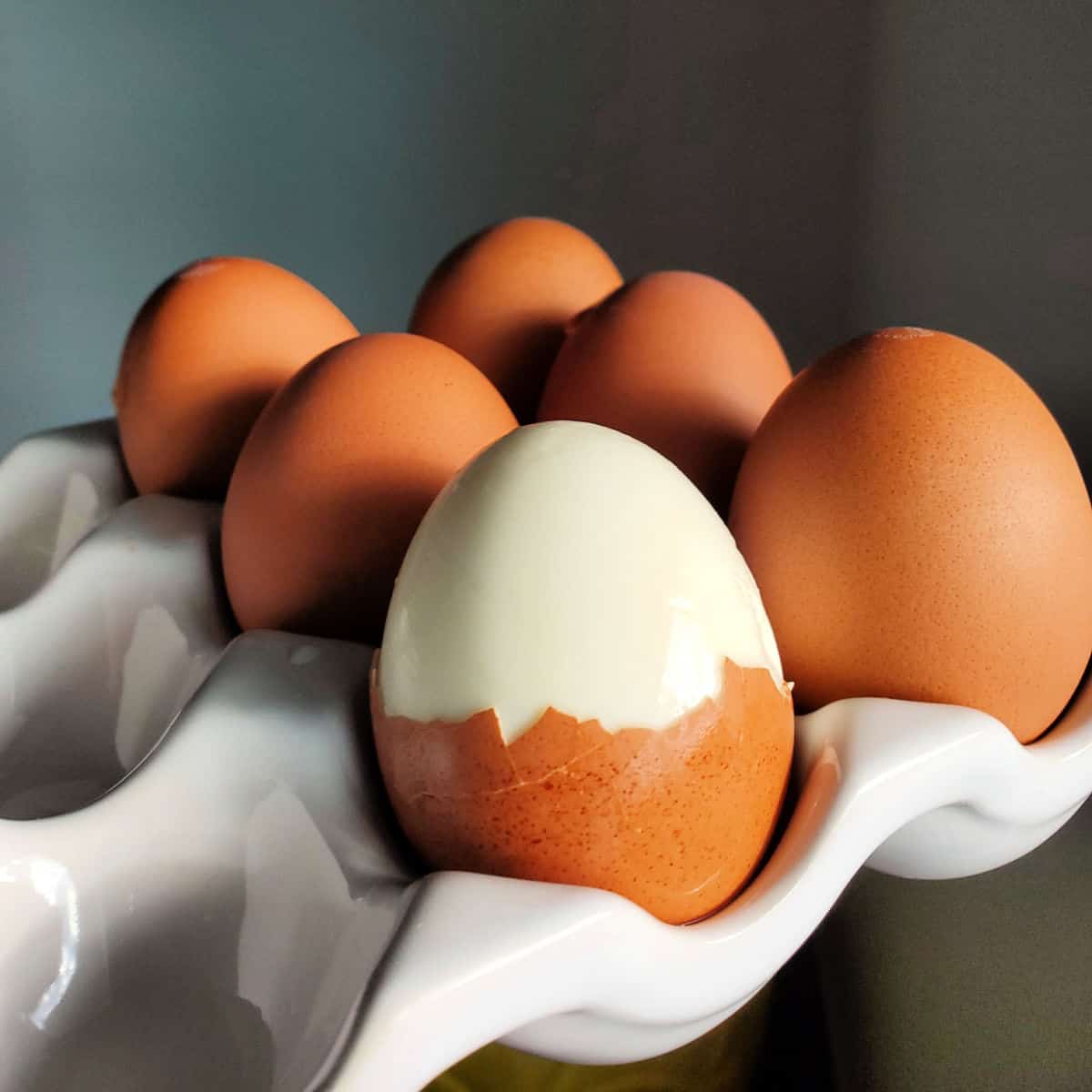 eggs in a white egg carrier with one of them partially peeled.