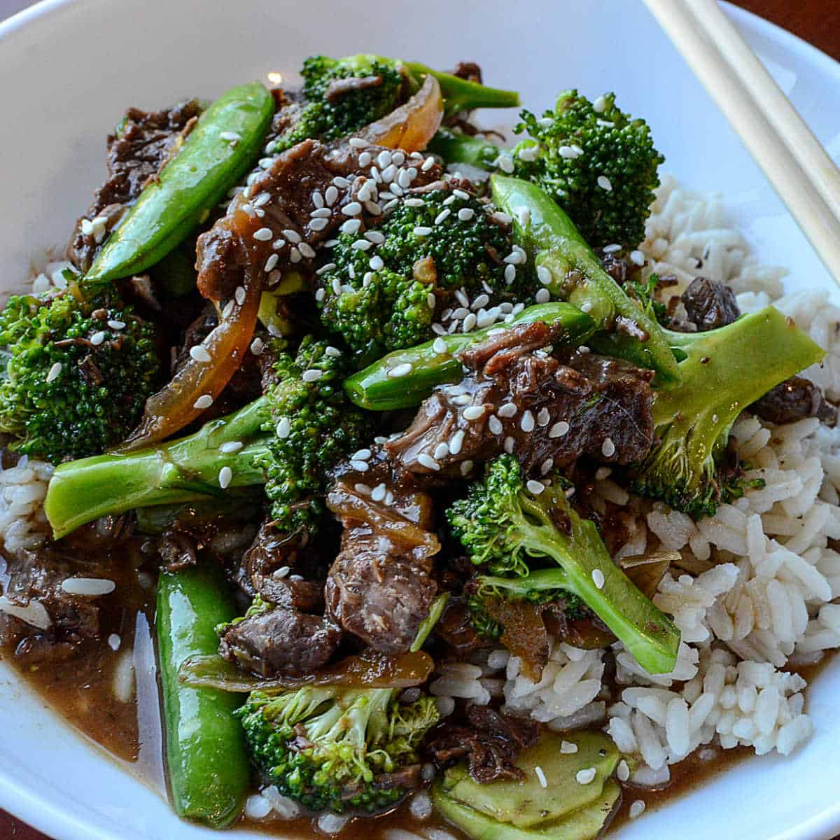 crockpot beef and broccoli in a white bowl with chopsticks