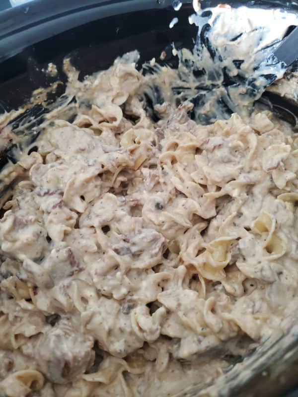 Crock Pot Beef Stroganoff in a black slow cooker with a black spoon