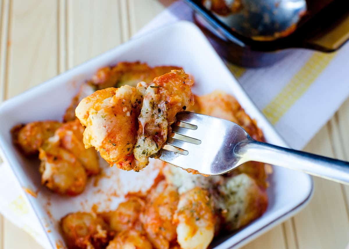 fork holding gnocchi casserole over a white bowl