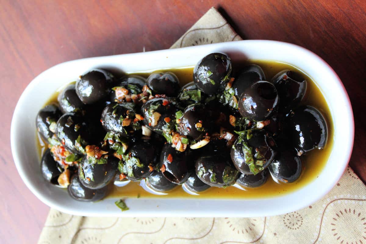 marinated olives in a white serving dish on a tan napkin