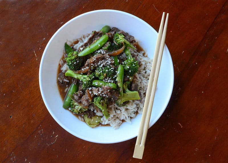 Slow cooker beef and broccoli over white rice in a white bowl with chopsticks