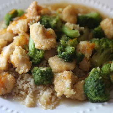 orange chicken and broccoli over a bed of rice on a white plate