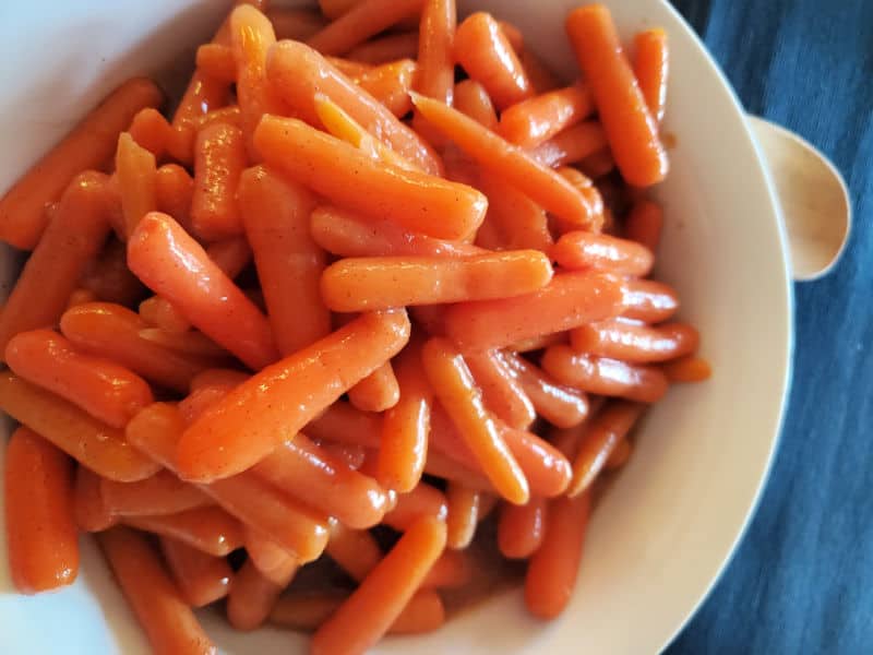 Glazed Carrots in crock pot in a white serving bowl with a wooden spoon. 